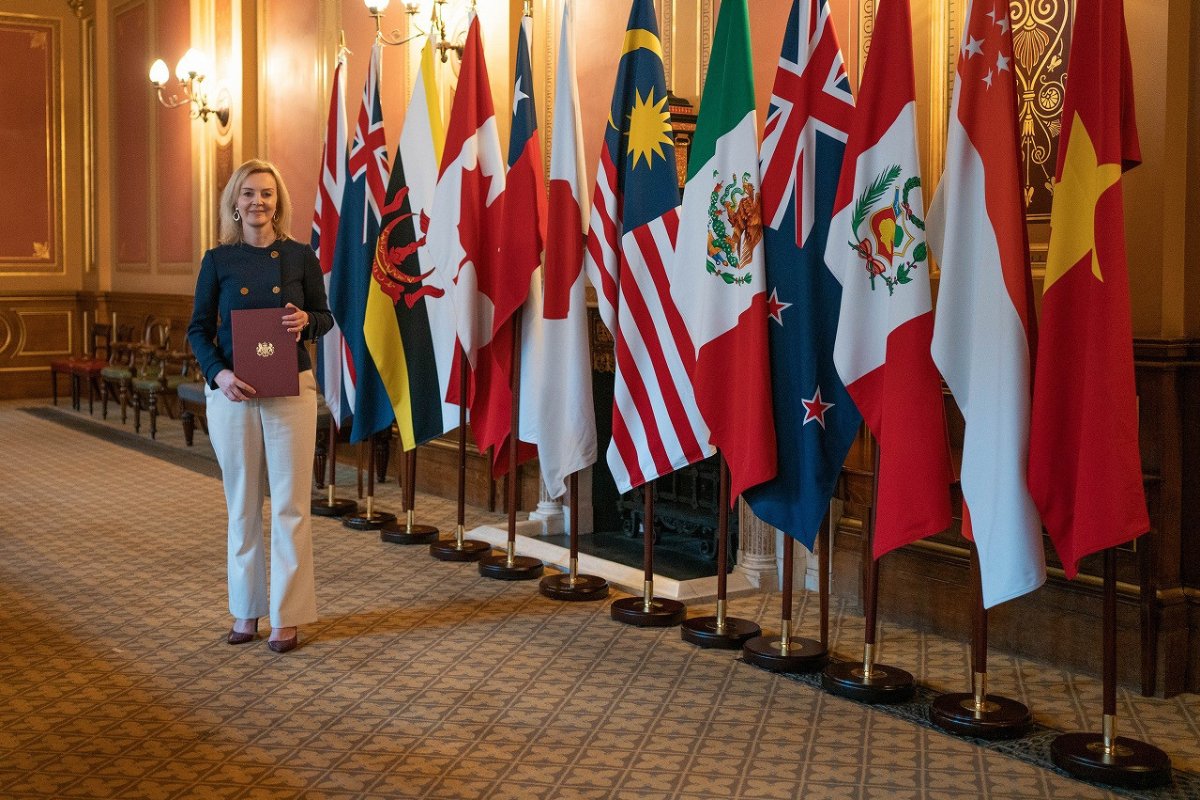 環太平洋連携協定（ＴＰＰ）参加国の旗の前で、参加申請の文書を手にするトラス英国際貿易相［英政府提供］