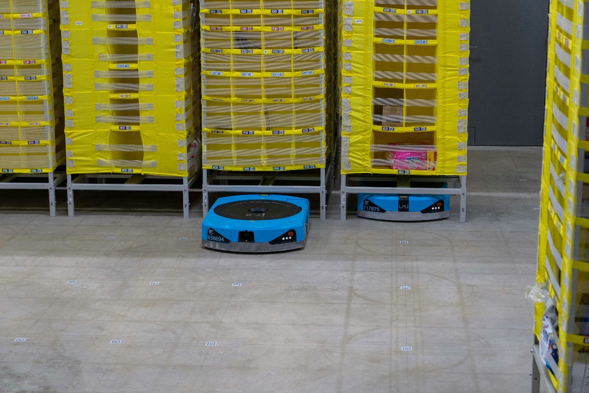 アマゾン・ドット・コムの千葉市の物流拠点に導入された自走式搬送ロボット（中央）。商品が入った棚を持ち上げて施設内を移動する［同社提供］